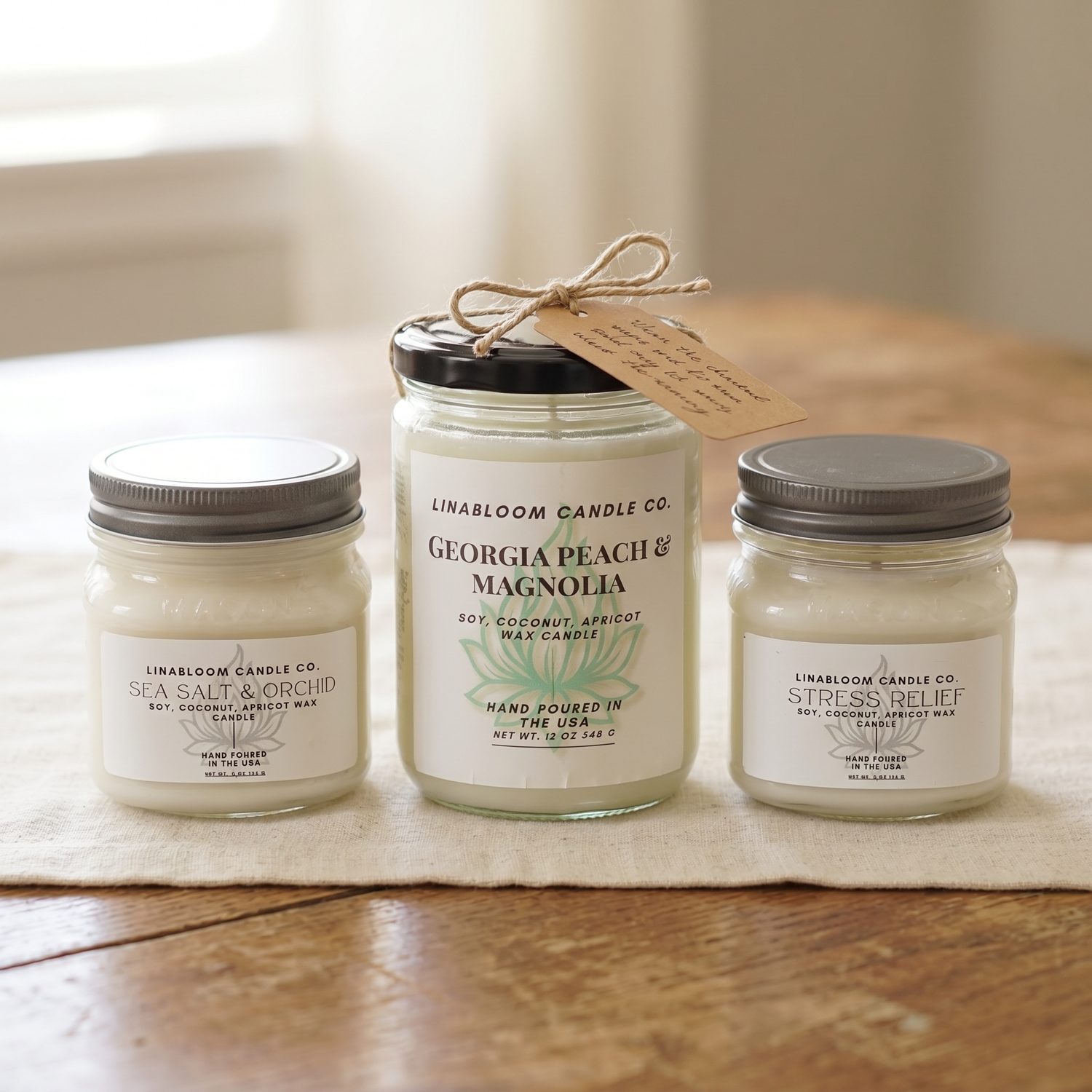 Bestsellers collection — Georgia Peach Magnolia, Sea Salt & Orchid, and Stress Relief on a cream linen runner with a kraft hang-tag