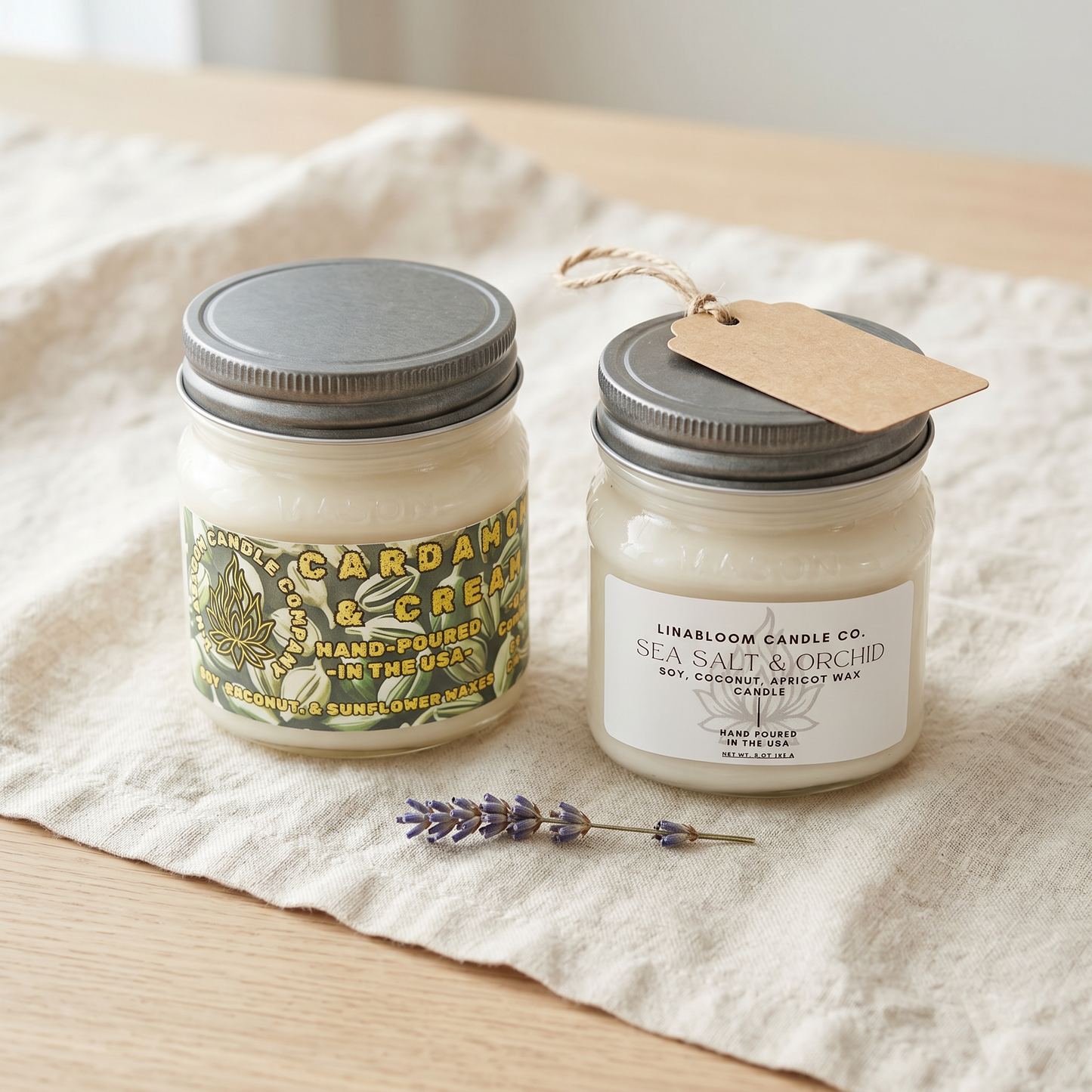 Two LinaBloom 8oz mason jar candles — Cardamom & Cream and Sea Salt & Orchid — with a kraft hang-tag on linen