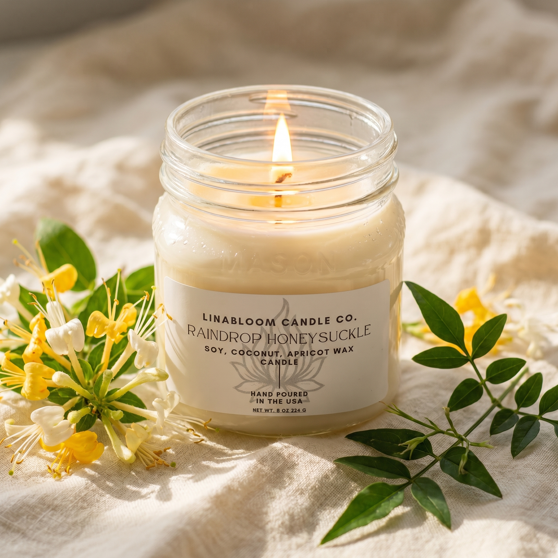 Raindrop Honeysuckle 8oz LinaBloom candle lit, with honeysuckle blossoms and jasmine on soft cream linen