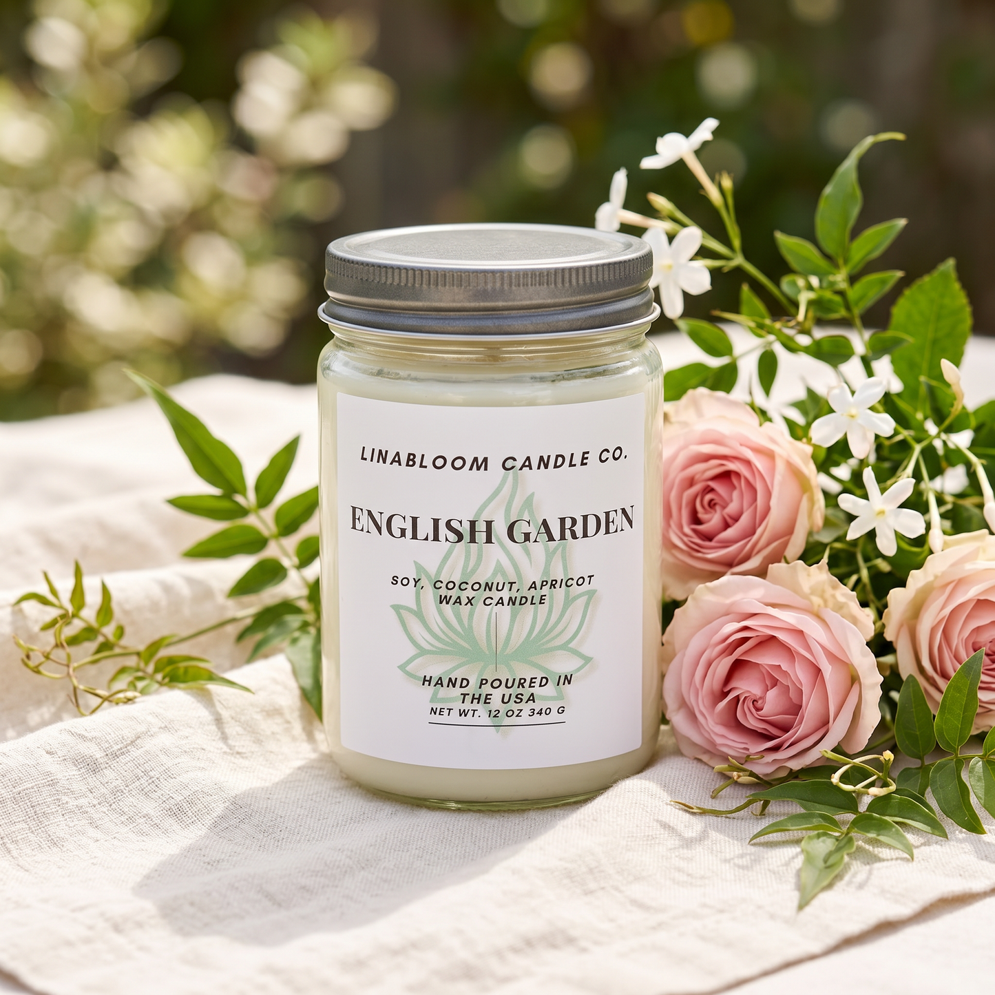 English Garden 12oz LinaBloom candle on cream linen with fresh pink roses and jasmine in a sunlit garden