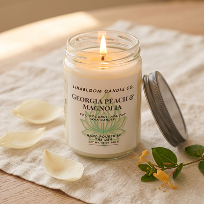Georgia Peach Magnolia 12oz LinaBloom candle lit, with honeysuckle and magnolia petals on cream linen