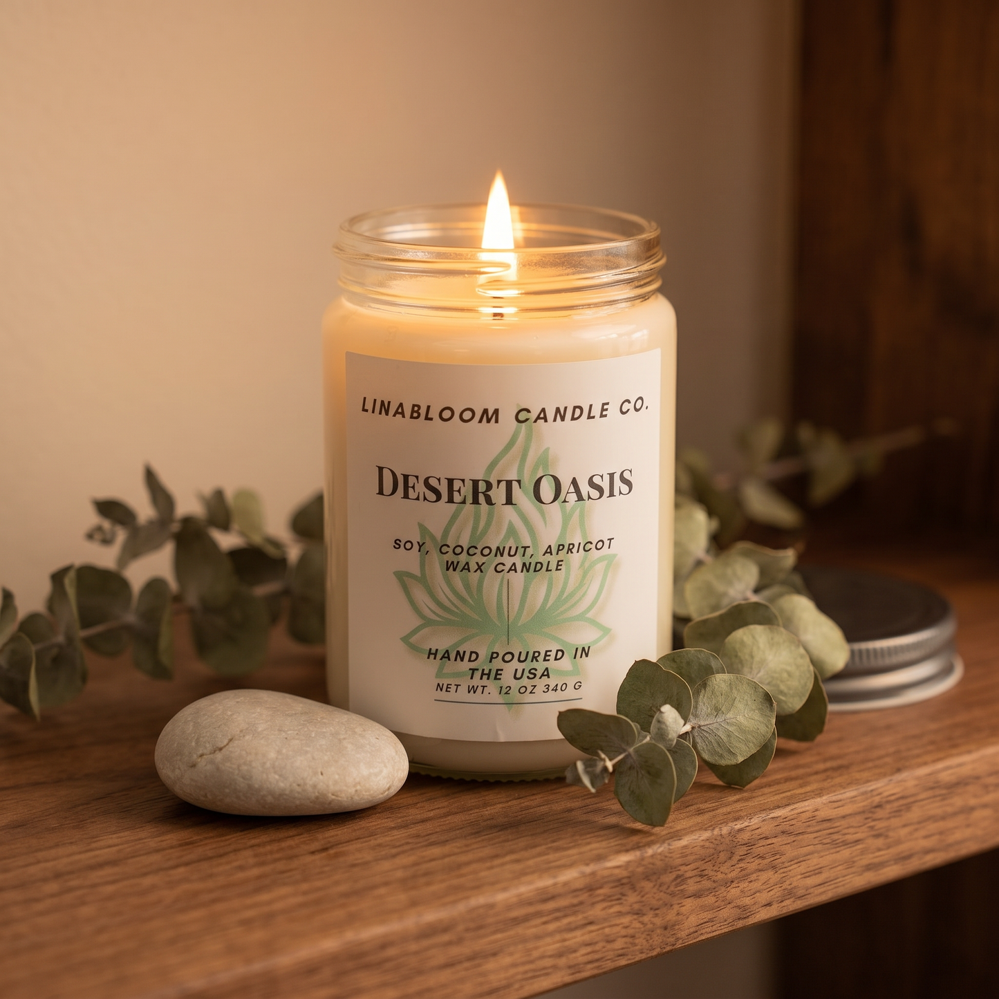 Desert Oasis 12oz LinaBloom candle lit on a walnut shelf with dried eucalyptus and a smooth stone